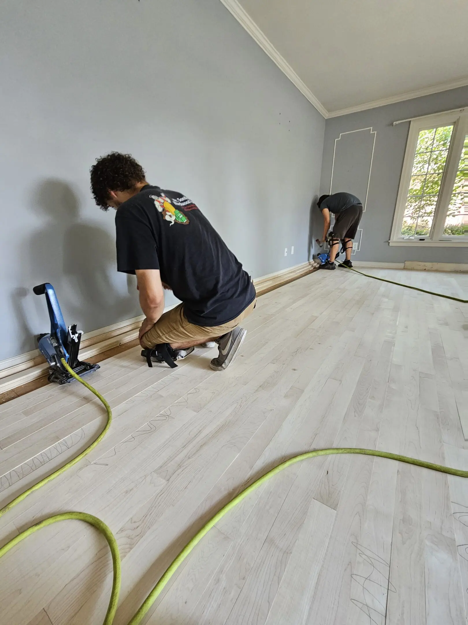 Two men are working on a hardwood floor.